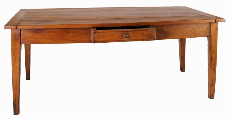 This 19th century French cherrywood farm table has a four board top with breadboard ends.  It has a centre drawer with ogee molding and original wood knob.  The table has a rich patina.  
The legs are tapered. 
Measure: Apron H 23.5