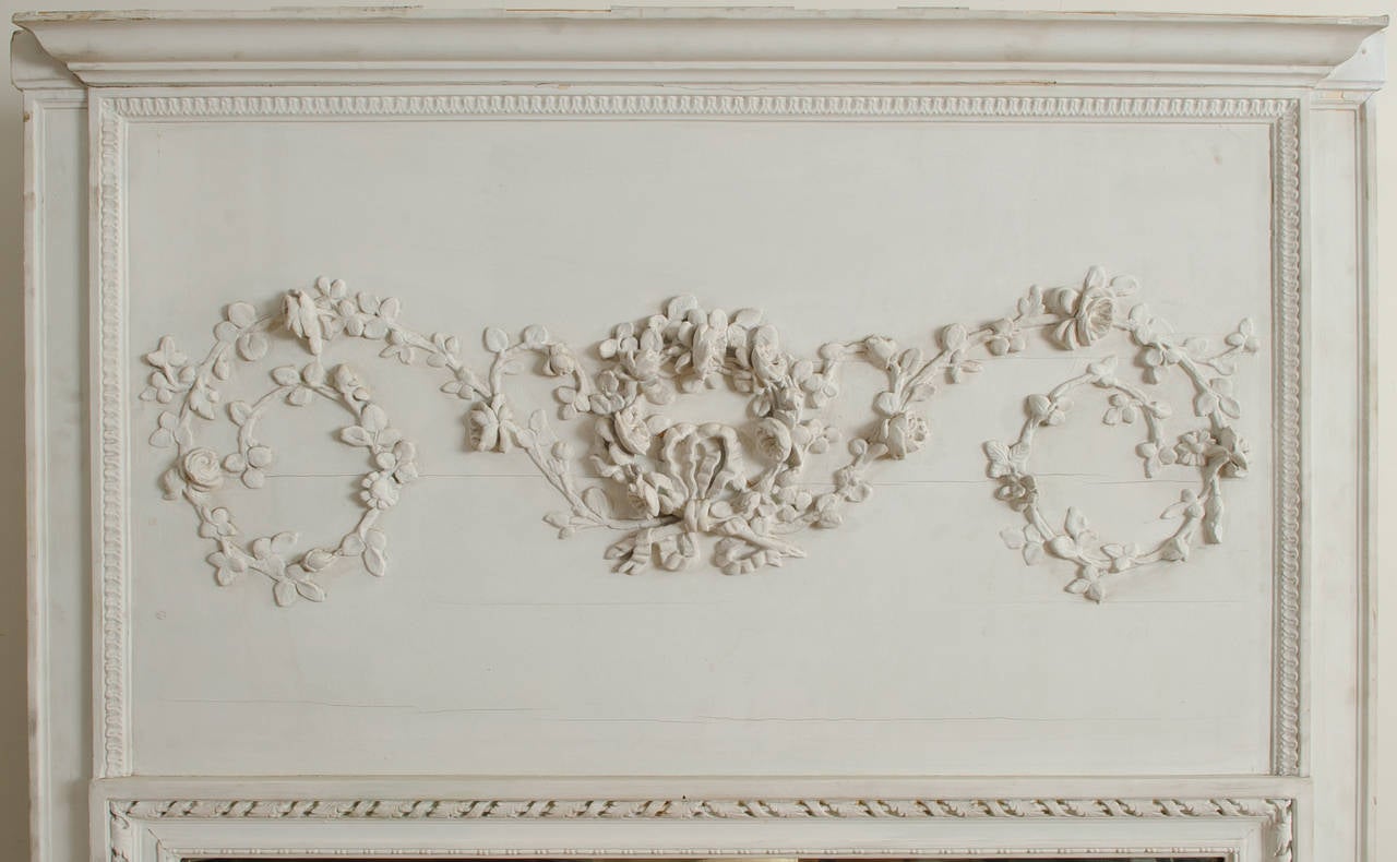 This Louis XVI trumeau mirror is one of two mirrors that are from the same paneled room in a chateau in southwest France. They have the same ring garland and bow applique´ and moldings, but differ slightly in size. This decorative panel is framed