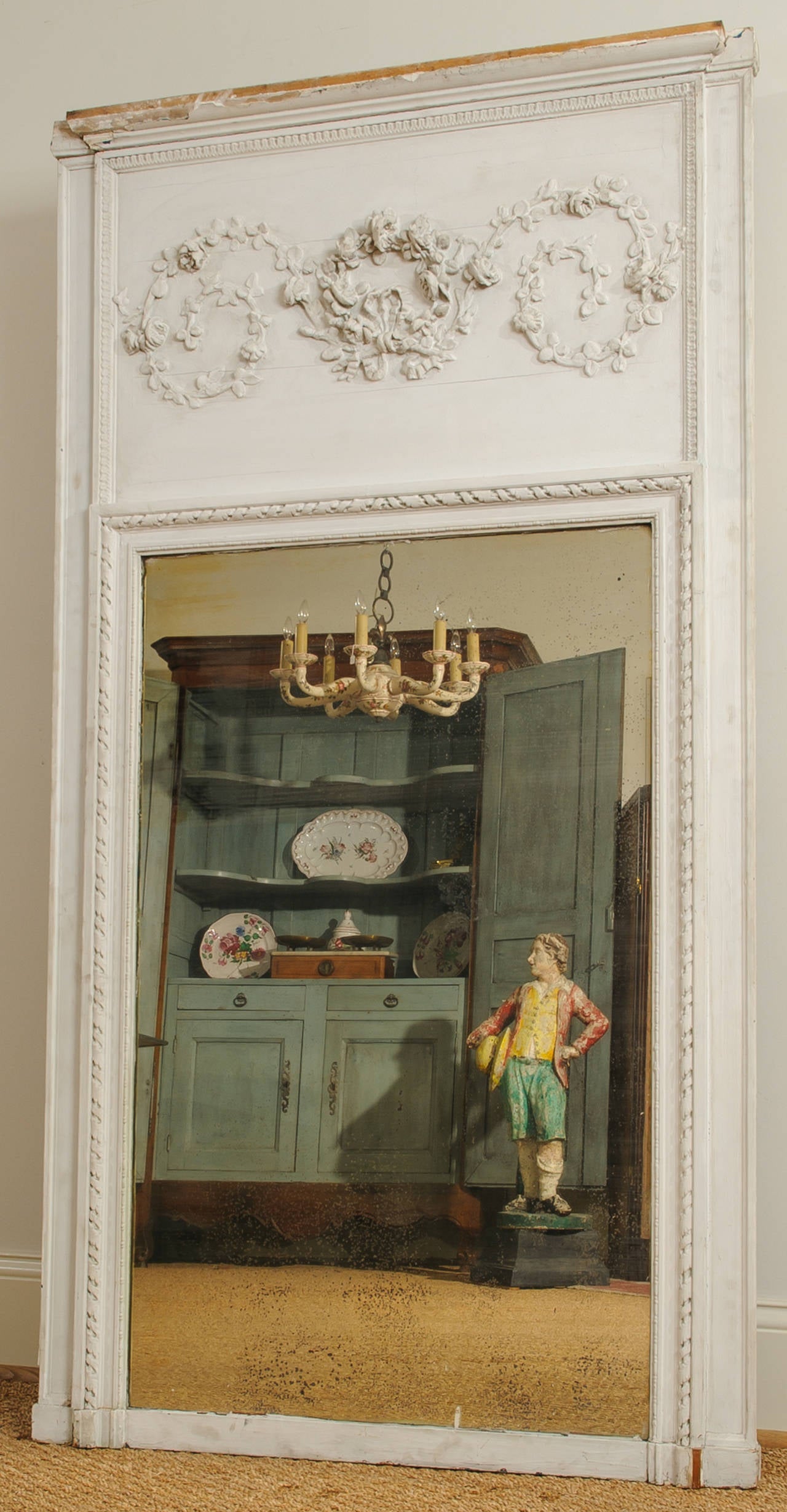 This Louis XVI trumeau mirror is one of two mirrors that are from the same paneled room, in a chateau in Southwest France. They have the same ring garland and bow applique´ and moldings, but differ slightly in size. This decorative panel is framed