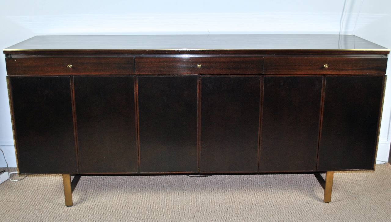 Stunning walnut credenza, cabinet by Paul McCobb featuring black leather folding doors, three drawers and brass trim details. Doors reveal shelves and ample storage space. Newly refinished in deep chocolate, makers mark inside drawer. Original