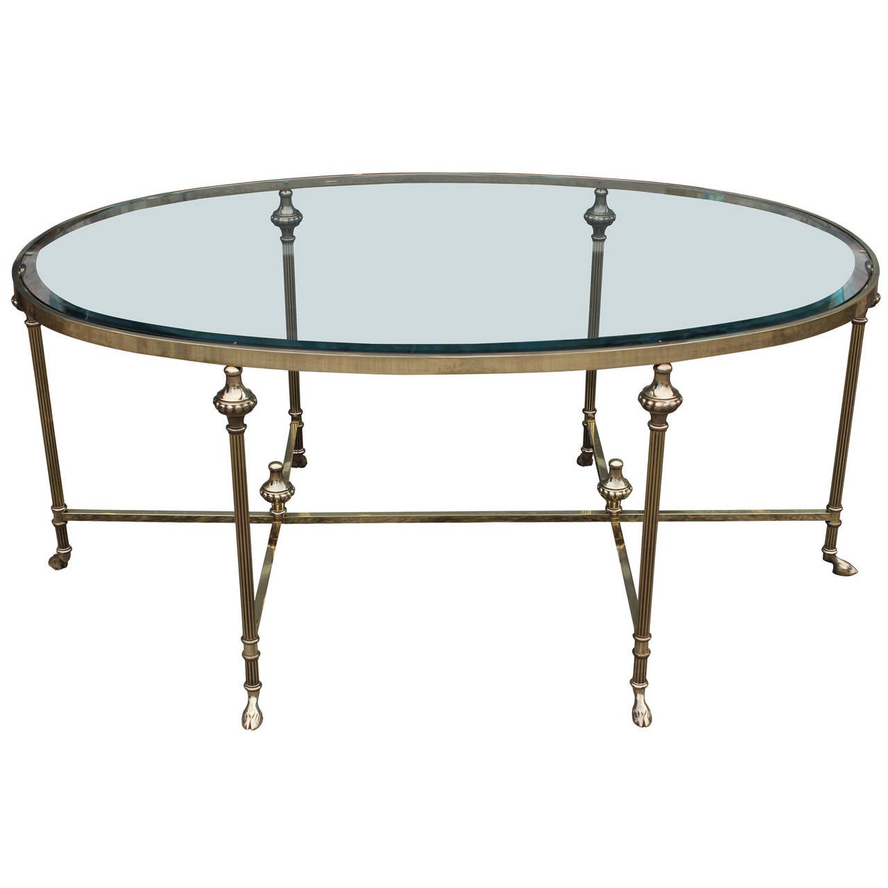 Luxe French brass and glass oval shaped coffee or occasional table. Hollywood Regency style table is finished with hoof shaped feet. Glass top rests upon brass finials. In the style of Maison Baugues. Great detailing.