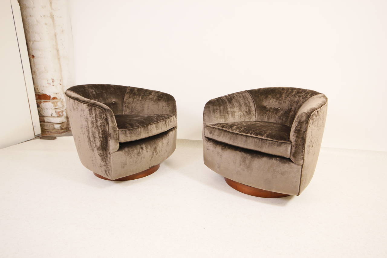 A glamorous and well balanced pair of swiveling and tilting, newly upholstered barrel-back lounge chairs having encircling forms rising from circular walnut disc bases. Designed by Milo Baughman for Thayer Coggin, circa 1960s.