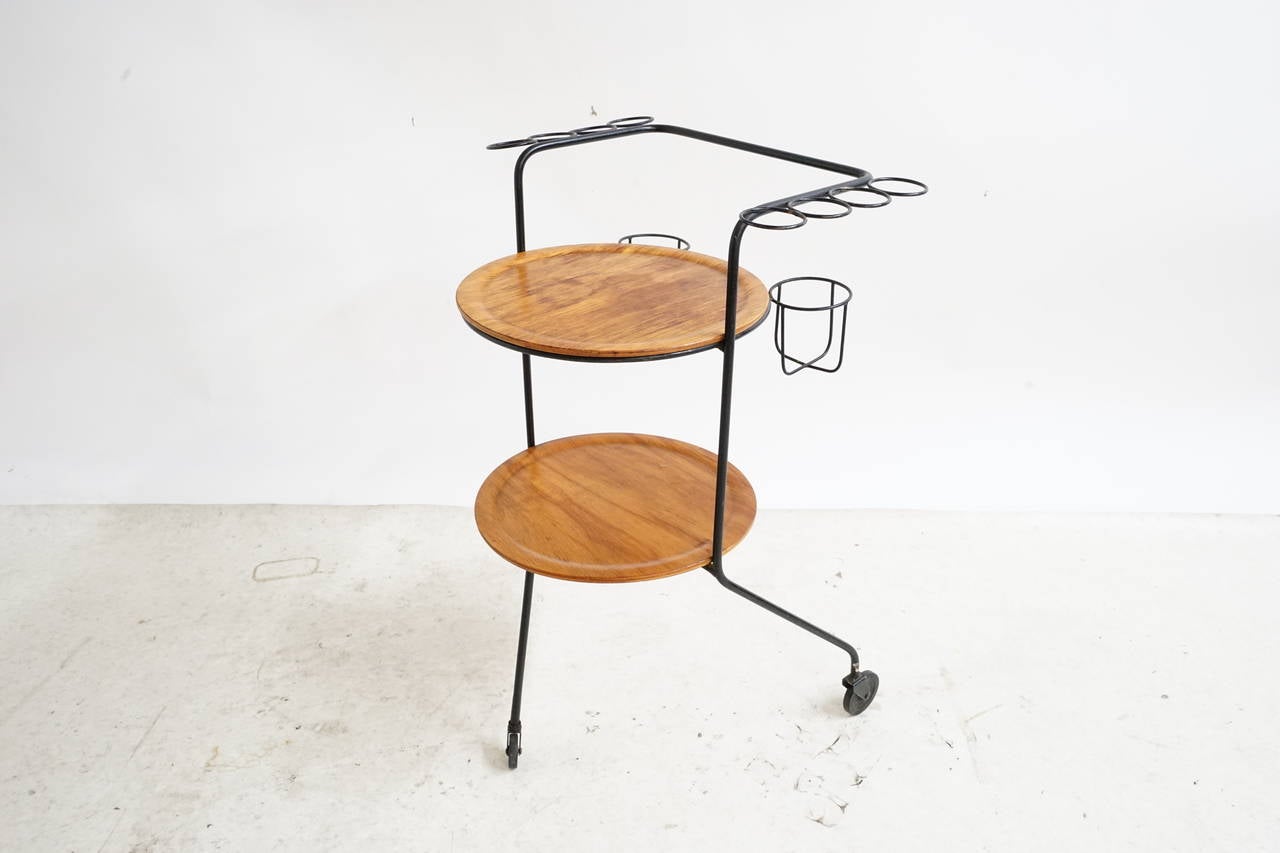 Gorgeous Two-tier rolling bar cart in wrought iron black metal,  Eight glass holders, two bottle holders, and wood shelves that remove for serving trays, Designed by Tony Paul, USA, 1950s.