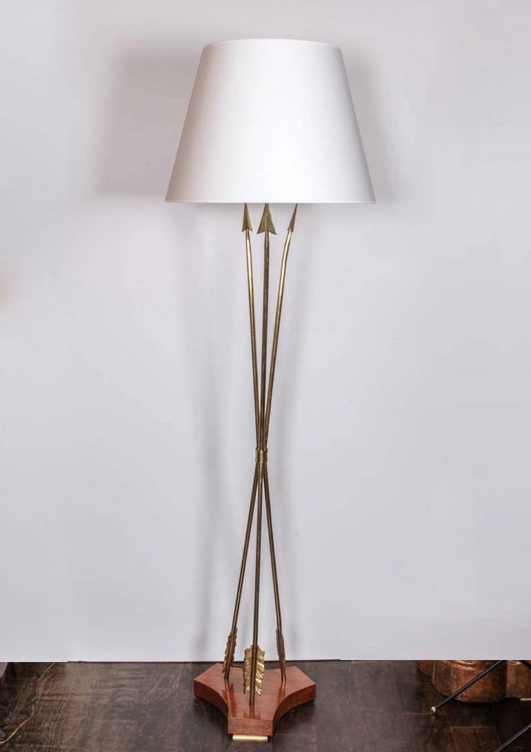 A late 1940s French floor lamp, with three brass arrows and a fruitwood base mounted on brass feet.