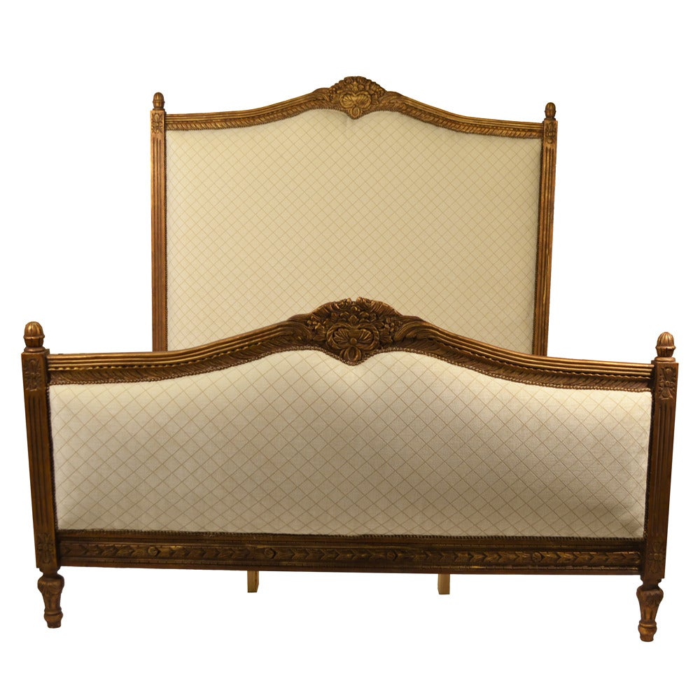 Louis XVI king-sized gilded bed with fluted posts, also featuring hand-carved center medallions with leaves and flowers.This bed is newly upholstered in a cream velvet fabric with taupe diamonds and custom slat frame. Antique brass nailheads add a