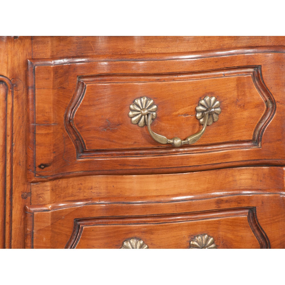 Period Country French cherry wood serpentine shape commode with cabriole legs and scroll carved feet, c. 1780. This commode features detailed hand carving around each drawer pull, as well as around each centered keyhole. All original antique brass