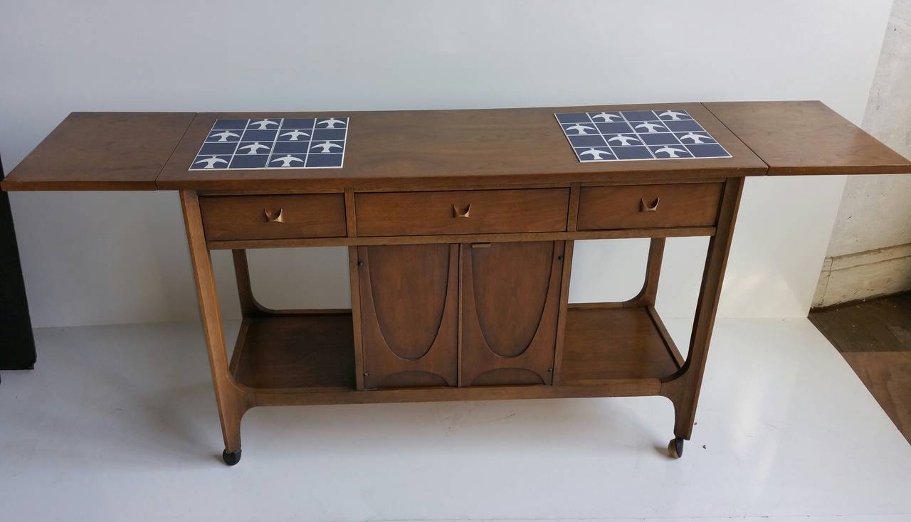 Mid Century Modern Broyhill Brasilia serving cart was designed by Oscar Niemeyer.  Original royal blue tiles with white birds .
 bar or buffet. The tiles act as trivets, protecting the walnut wood. Two drop leaf extensions allow one to expand the