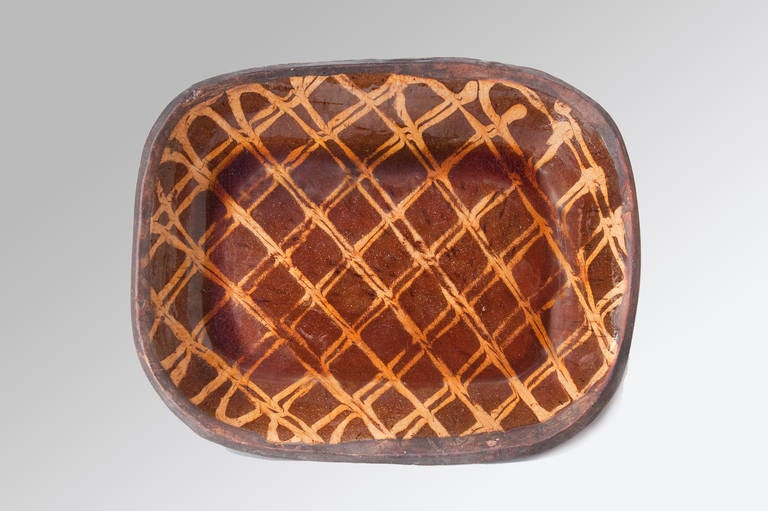 A large and handsome 18th century Slipware baking dish with a plain edge being an orange/brown colour and having buff coloured trailed and combed slip decoration in a lattice pattern, the glaze having been wiped at the edges.
This large antique
