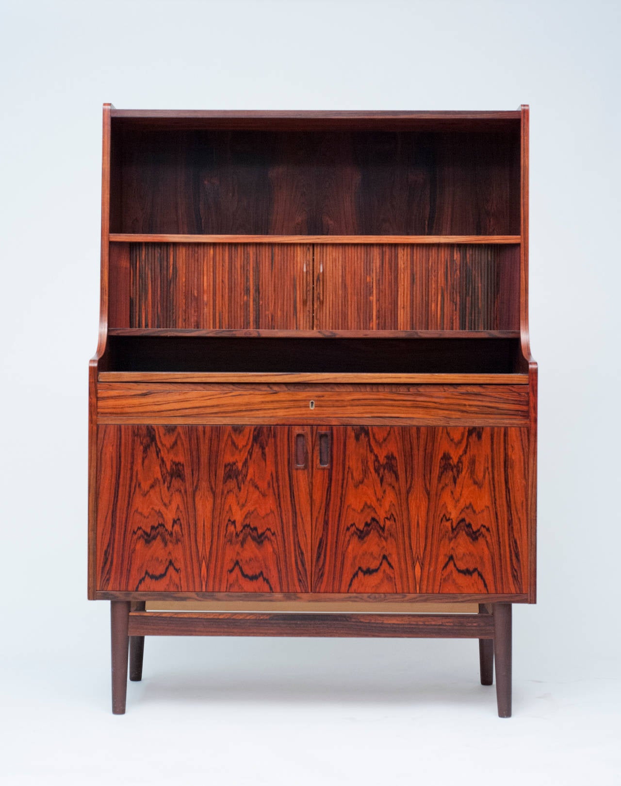 Attractive and functional rosewood Secretary by Bornholm Mobler of Denmark.  Tambour doors retract to reveal three drawers, one of which contains a mirror.  Writing desk can be pulled out or retracted when not in use. Secretary is complete with