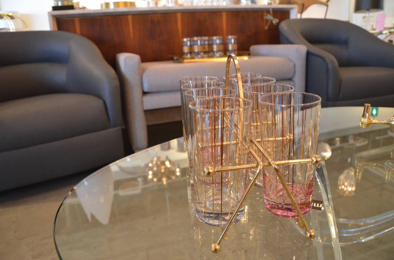 A stunning set of eight Tom Collins glasses with 22-karat gold vertical stripes featuring color flashed bases two each in light blue, amber, rose, and lilac. The set is housed in a loop handled caddy of bent brass plated rods with ball finials and