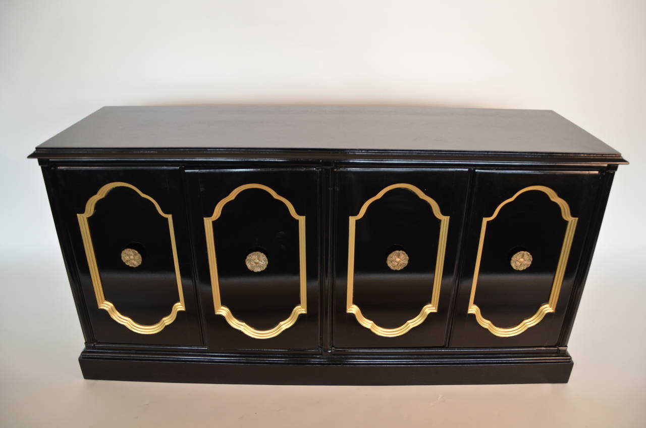In the manner of Dorothy Draper, lacquered black and gold sideboard with oversized decorative brass pulls.