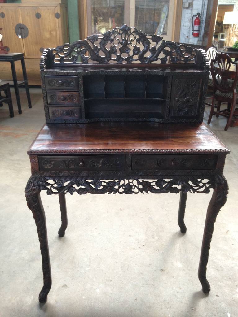 A Chinese Carved Rosewood Writing Desk, in two parts, the block front superstructure having a pierce carved gallery, one long drawer, three short drawers and a panel door carved with ancient symbols of good will: bats, clouds and dragons in relief,