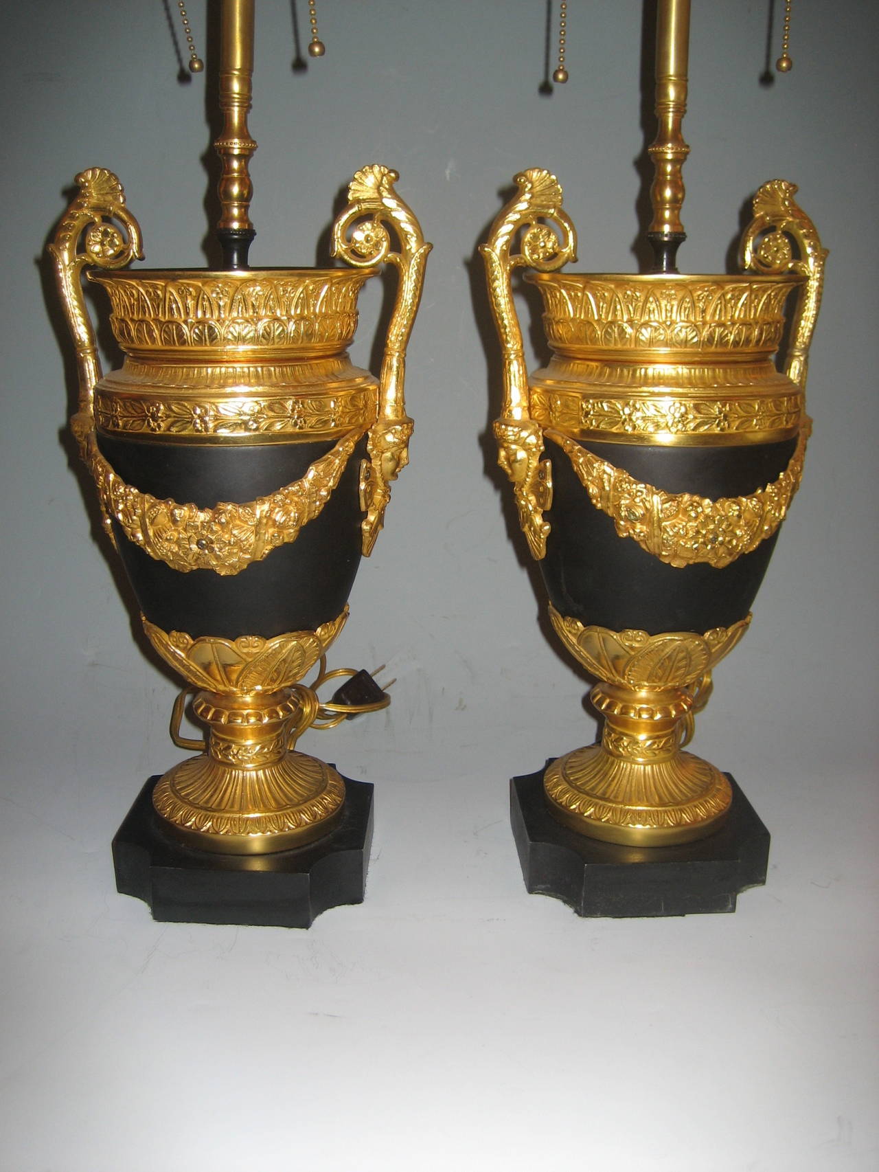 A Pair of Antique French Empire Style Neoclassical gilt bronze & patina bronze lamps embellished with figural masks.