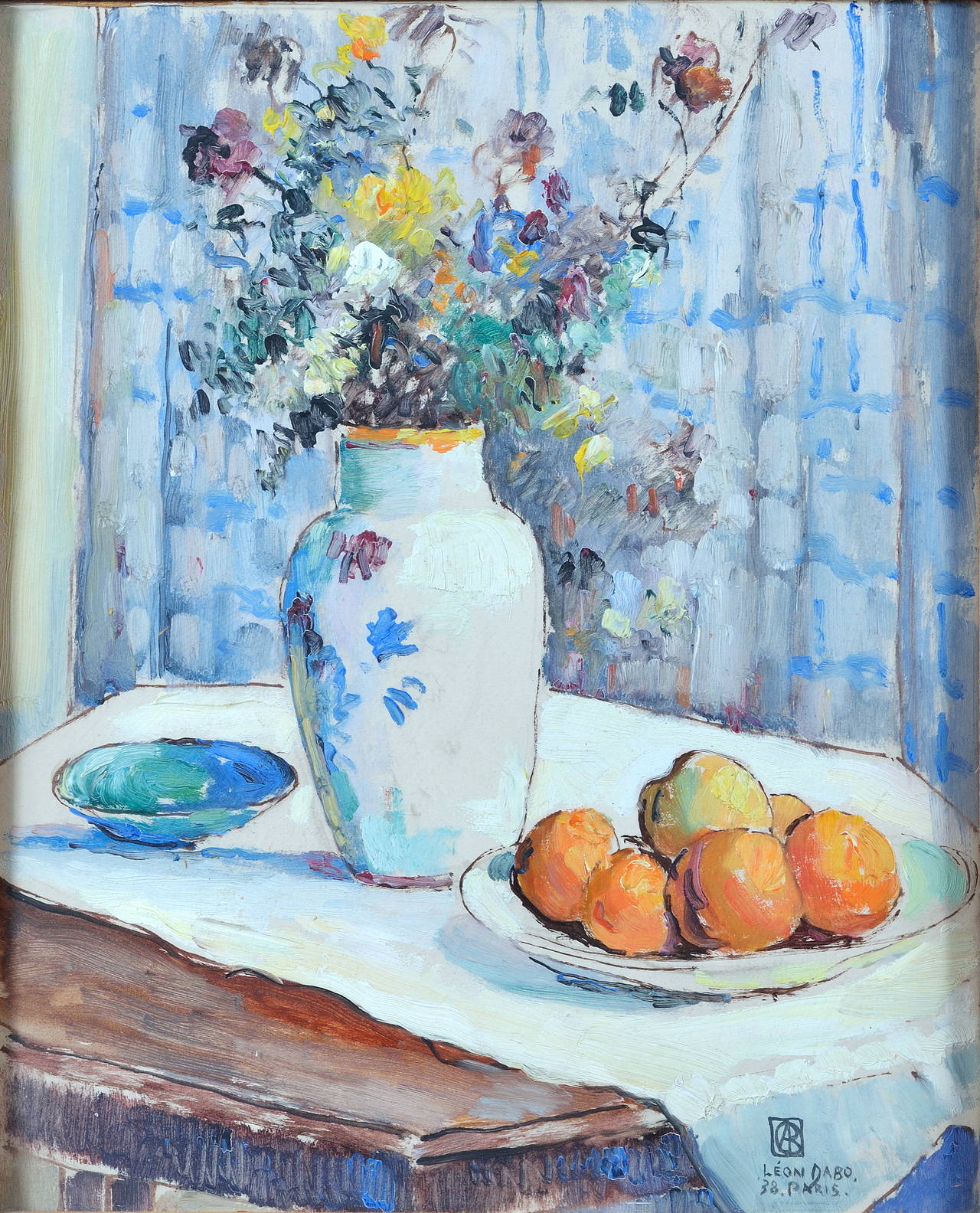 Leon Dabo (American, 1865-1960).
Lovely and fresh painting with wildflowers in a vase, peaches and a blue faience bowl on a table covered with a fine white linen against a curtain with blue patterns.
1938.
Oil on cardboard with protective