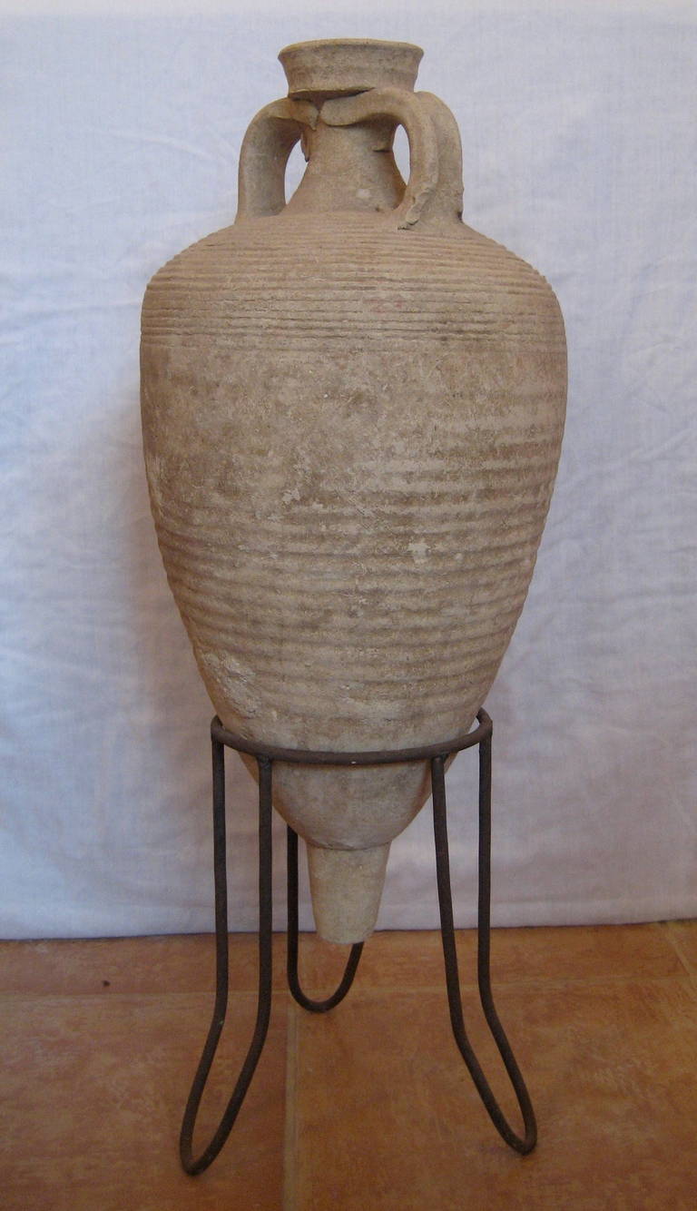 An Eastern Mediterranean (Palestinian) pottery wine-Amphora.
With collared rim; strap-like handles grooved on their outer surface; body tapering towards a solid knobbed toe.
Orange-brown clay with lime deposit.
Body covered with shallow regular