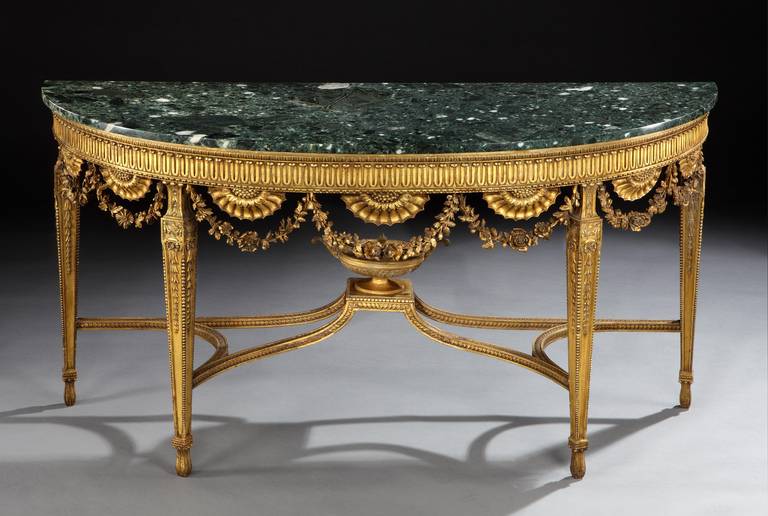 A George III style giltwood demilune pier table, the verde antico marble top above a carved frieze with sunflowers and swags of flowers, supported on tapered legs with a carved stretcher and central urn after a design by John Linnell for Shardeloes,