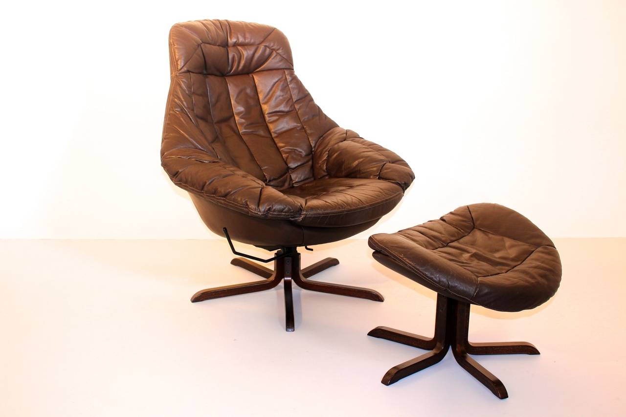 A very comfortable and stylish leather vintage lounge chair with an ottoman by Henry Walter Klein, 1970s, Denmark.
The lounge chair has rosewood swivel base and upholstered with brown leather. 
The leather surface has a beautiful leather patina,