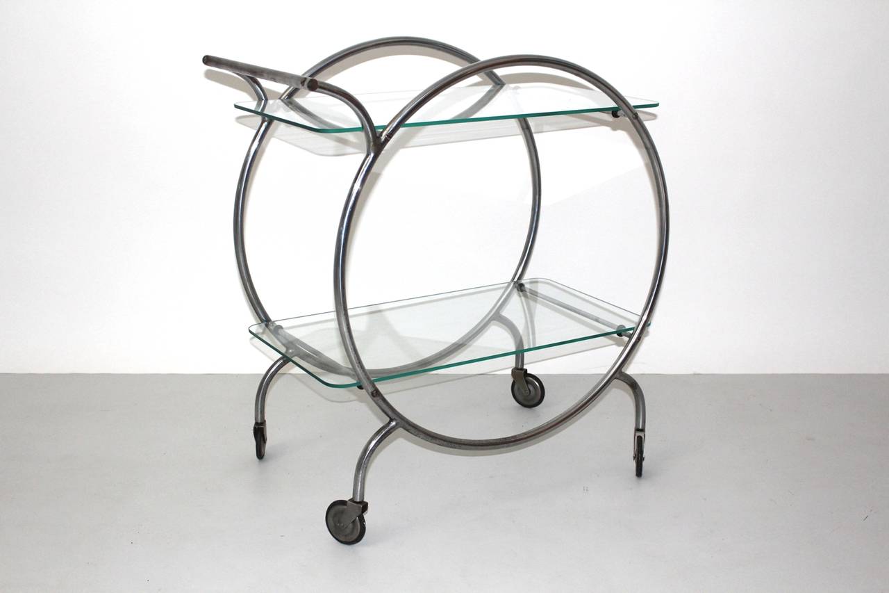 An Art Deco vintage metal bar cart attributed to Staatliches Bauhaus Dessau Germany circa 1928, which shows a chrome-plated round shaped frame with two clear glass shelves and four wheels.
We particularly love the bar cart for its clear and sleek