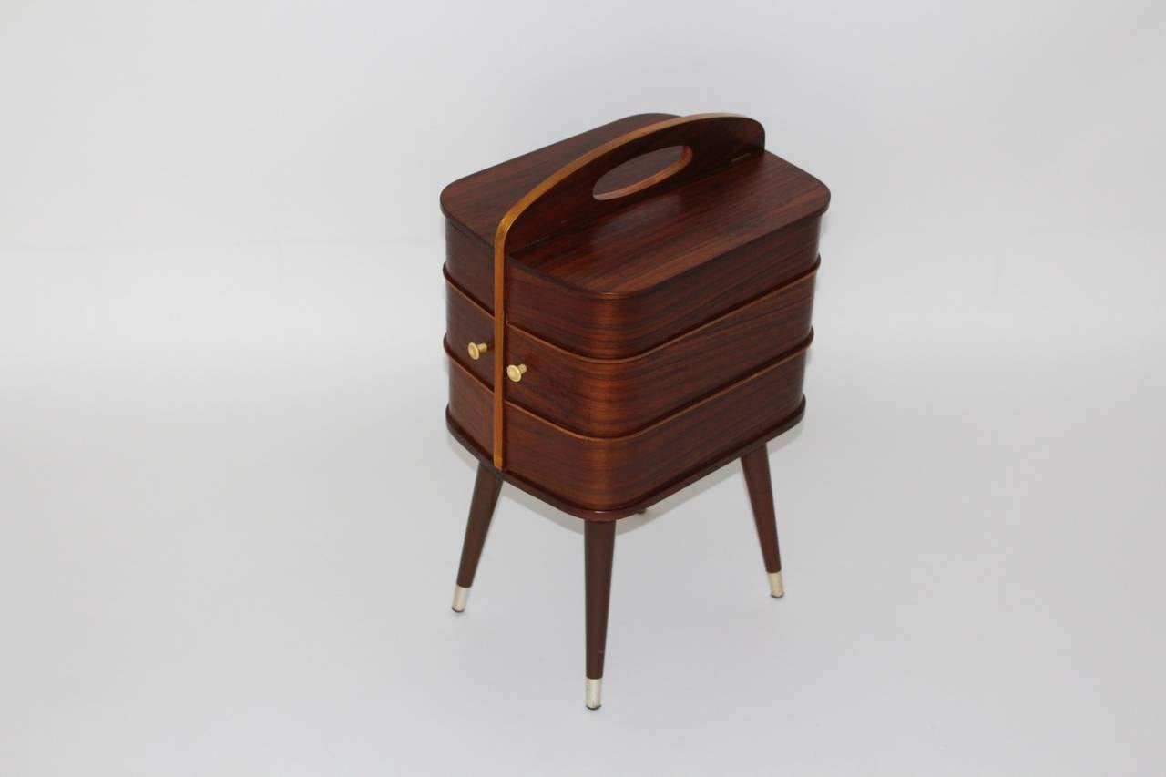 Lovely three-tiered wooden Mid-Century Modern sewing box or commode with two revolving drawers.
The drawers hide two storage boxes.
Also the upper section is divided in two parts and has two folders to open.
Additionally two buttons decorate this