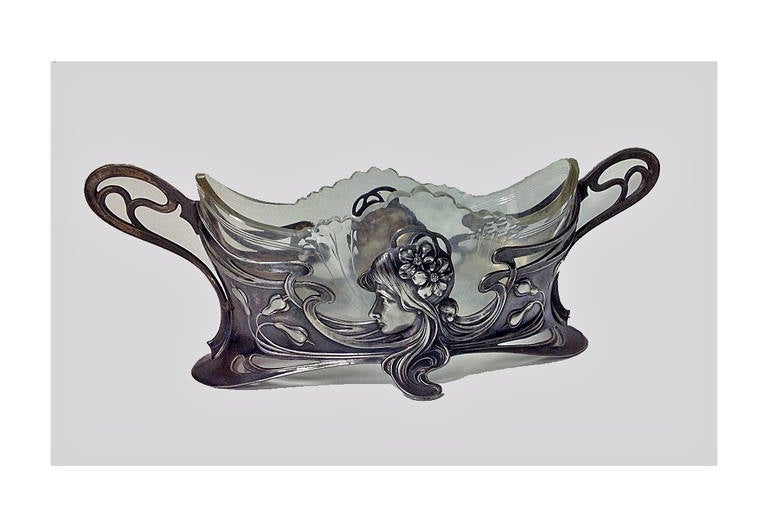 WMF Art Nouveau Jugendstil silver plate on pewter centerpiece, Germany, circa 1900. The centerpiece with Art Nouveau maiden decoration, original engraved glass liner. Marks: AS WMFB. Measures: 12 x 4 x 4 ¼ inches. Illustrated WMF 1906 catalogue page