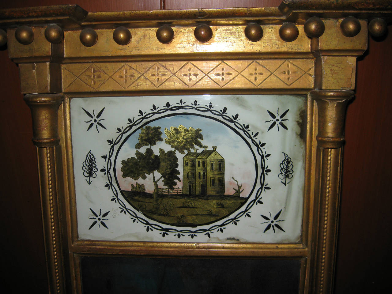 Miroir détaillé en bois doré églomisé ou peint à l'envers, datant du début du XIXe siècle et représentant une maison primitive à trois cheminées. Il provient d'une maison de Philadelphie et est en très bon état pour l'âge ; notez quelques pertes de