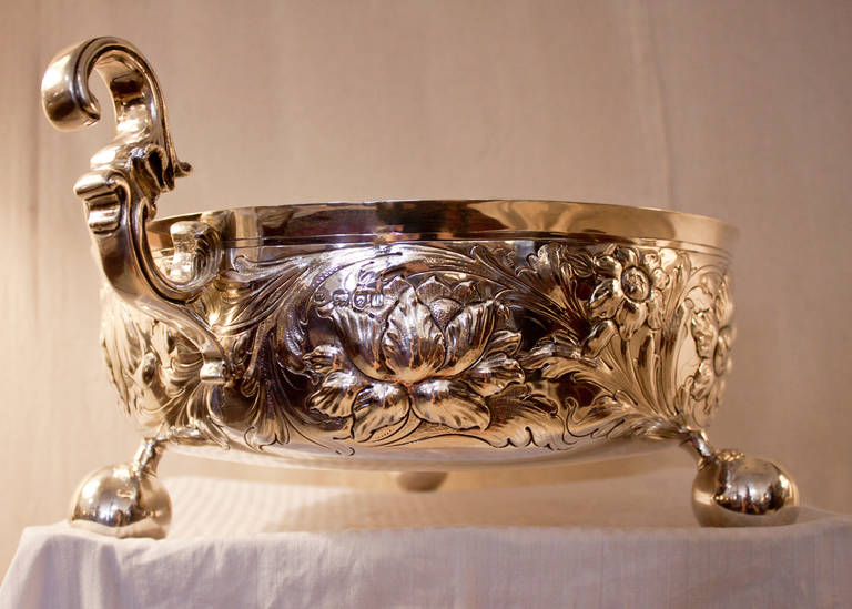 This gorgeous Art Nouveau English sterling silver bowl is used for cooling wine 
 and features a repose floral design with three exaggerated pedunculated knob feet and fanciful scroll handles. The handles are two inches higher than the bowl- (see