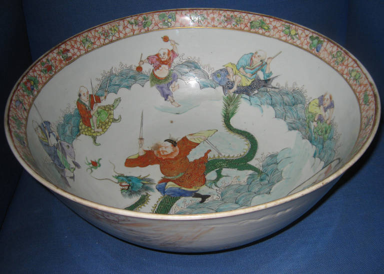 Chinese Export porcelain punch bowl dating from the 19th century featuring a double sword wielding warrior with a five-footed Royal dragon as the centerpiece inside the bowl. The warrior is flanked by eight figures riding waves and interacting with,