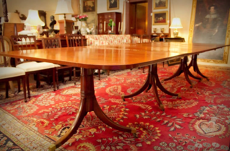 Cette table de salle à manger monumentale du XVIIIe siècle en acajou Sheraton anglais peut être rallongée par trois feuilles. Les quatre gracieux piédestaux sont dotés de pieds coiffés de laiton et de roulettes. Les piédestaux et les feuilles