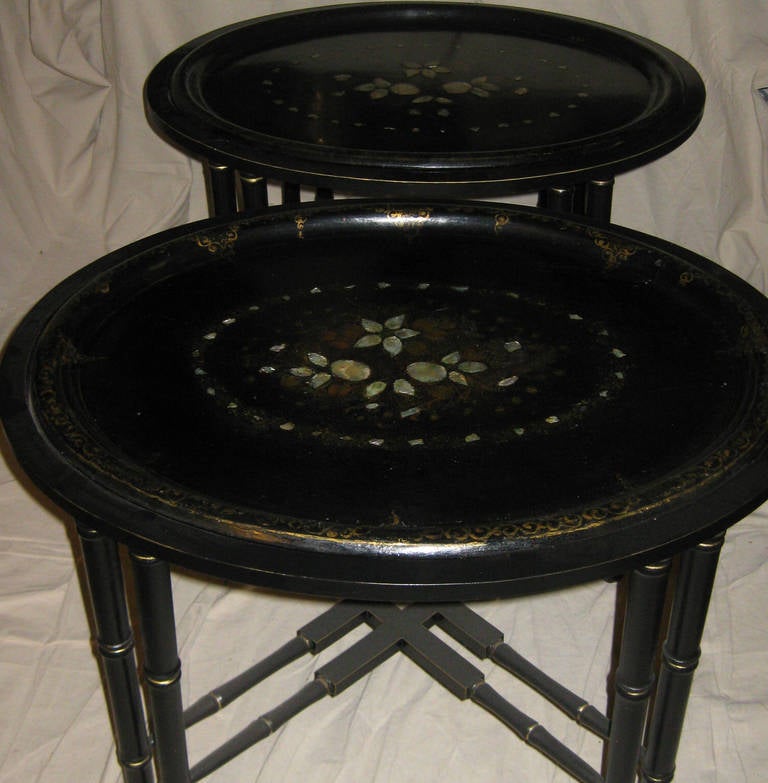 Twin papier mâché tray tables with removable trays featuring a floral design of abalone inlay with a gold gilt border. The black ebony simulated bamboo wooden bases were later added and were specially made with eight legs and double cross bars for