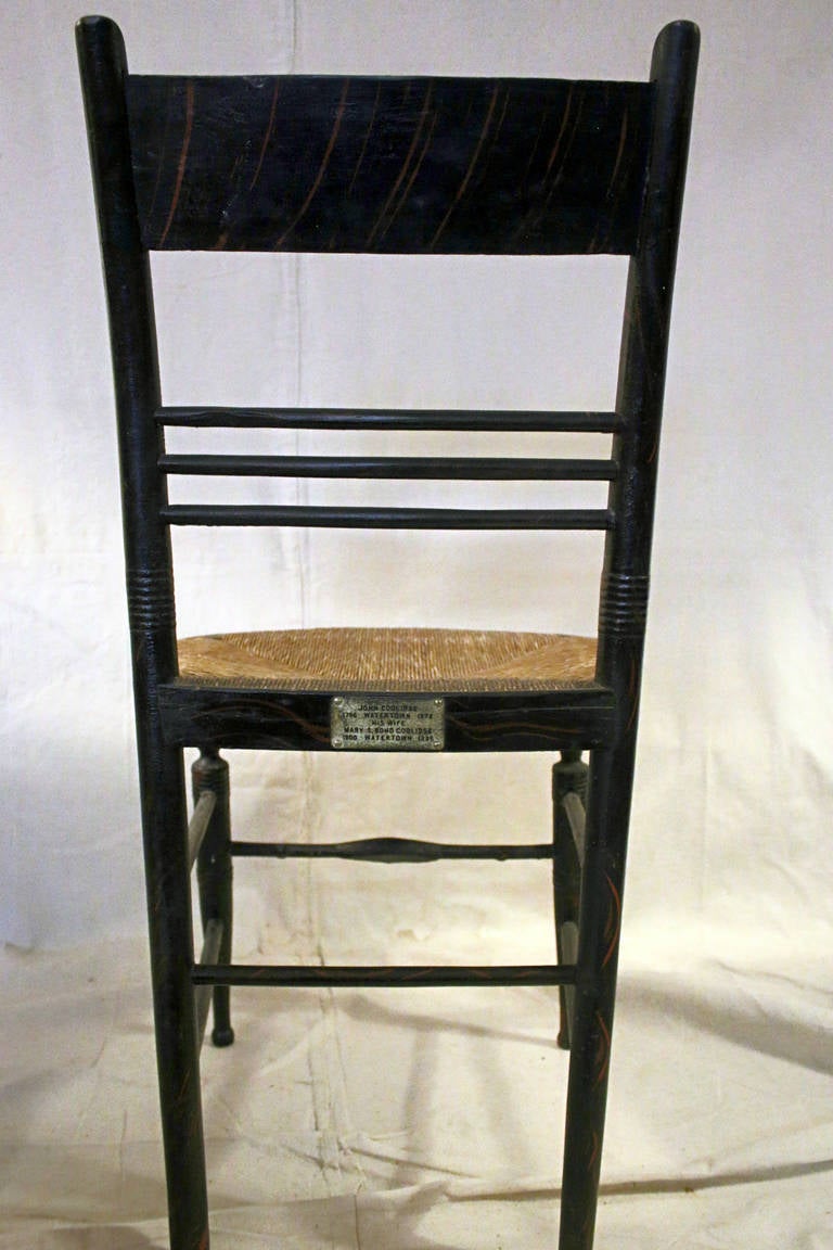 Early American chair from Connecticut decorated with gold stencil in a grape vine motif with red painted accents. In original condition with notched rush seat surrounded by steam bent seat rail. A commemorative metal plaque has been added to the