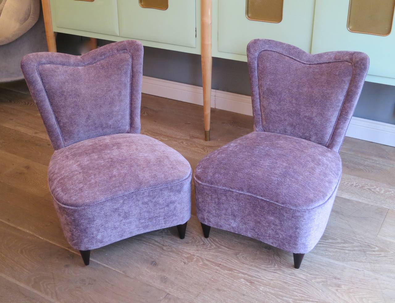 A pair of heart shaped slipper/bedroom chairs re upholstered  in purple textured Osbourne & Little fabric.
