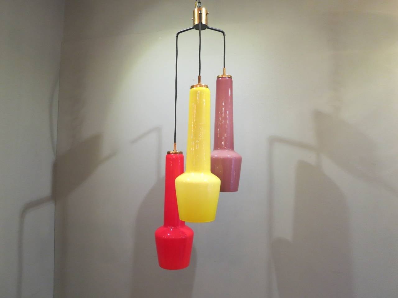 A Stilnovo pendant light with three colored glass shades in red, yellow and mauve. With brass fittings and newly wired black silk flex. Marked Stilnovo.