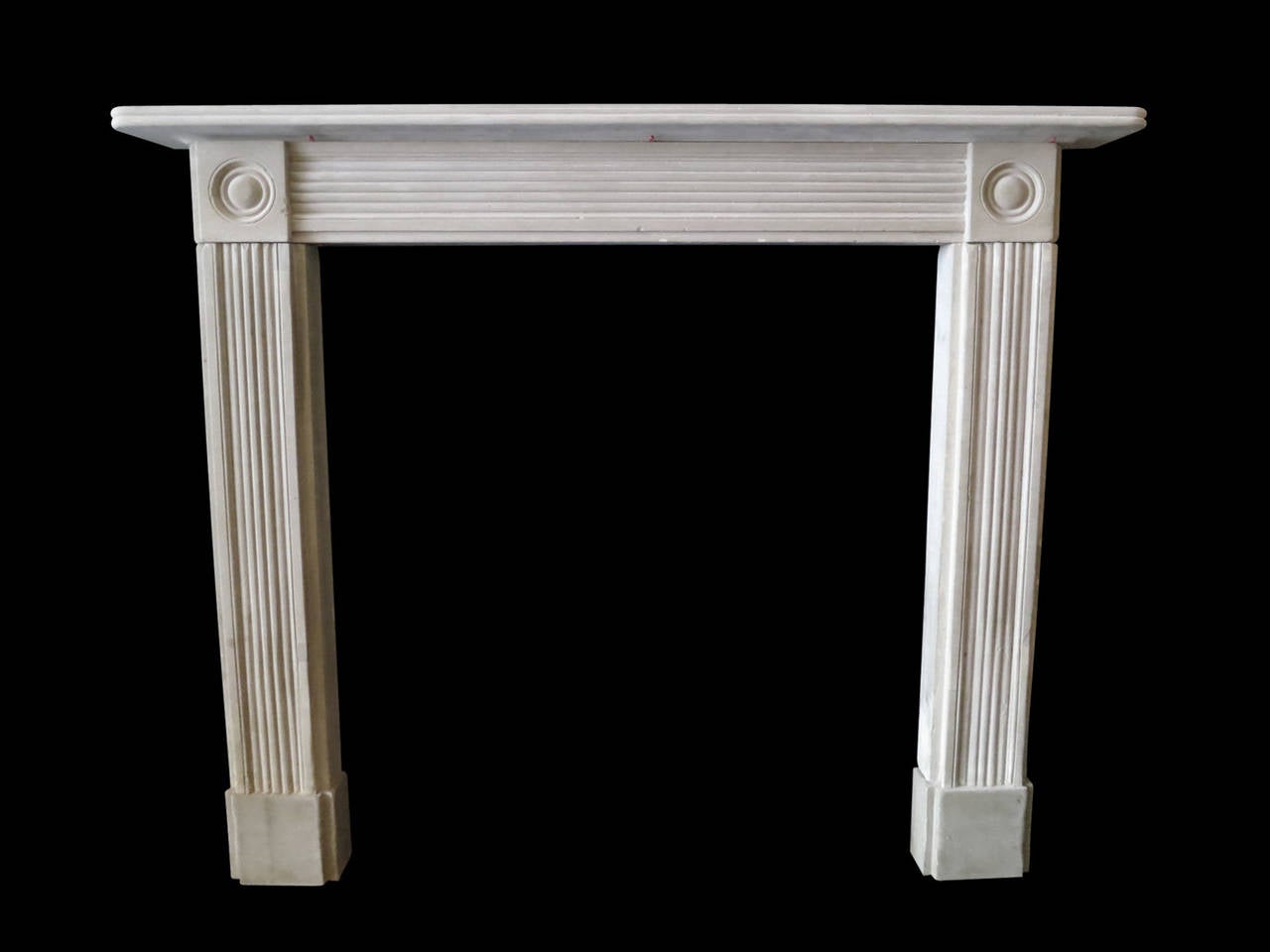 An English stone fireplace from the Regency period, with reeded jambs and frieze. Simple reeded shelf and carved roundel corner blocks. All standing on square foot blocks. Early 19th century.

Opening 90.5 cm W x 98 cm H.