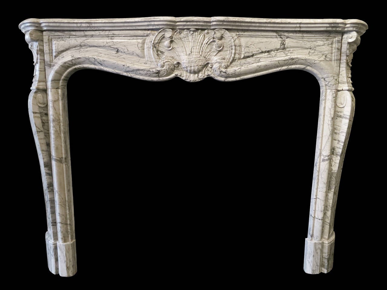 A Louis XV style fireplace in Bleu Fleuri a richly veined grey marble from Italy. The panelled frieze with finely carved cartouche to centre, the carved scrolled corner blocks of leaf and bell drop and serpentine shaped and molded shelf. A Fine