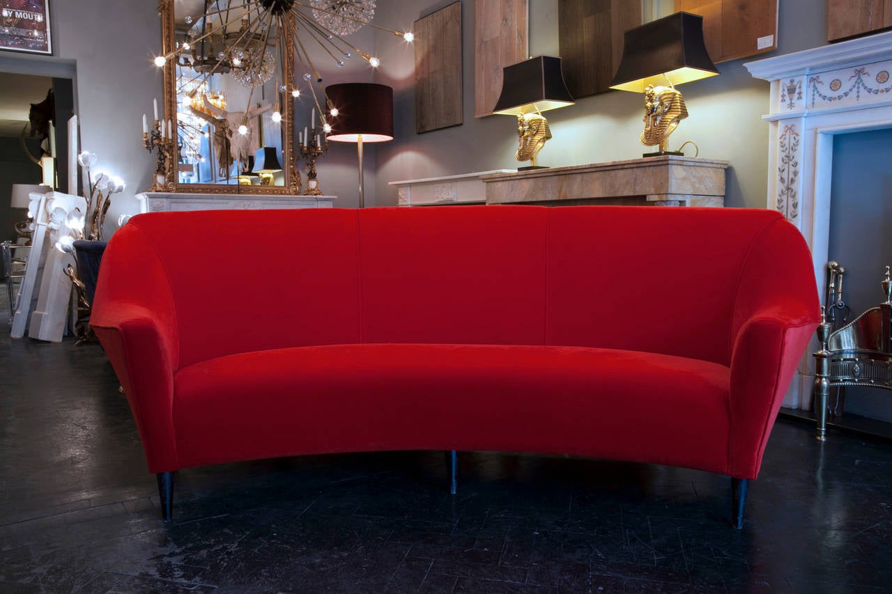 A large curved sofa in the manner of Ico Parisi. Re upholstered in red velvet on six ebonized turned wooden legs, with wide winged arms.