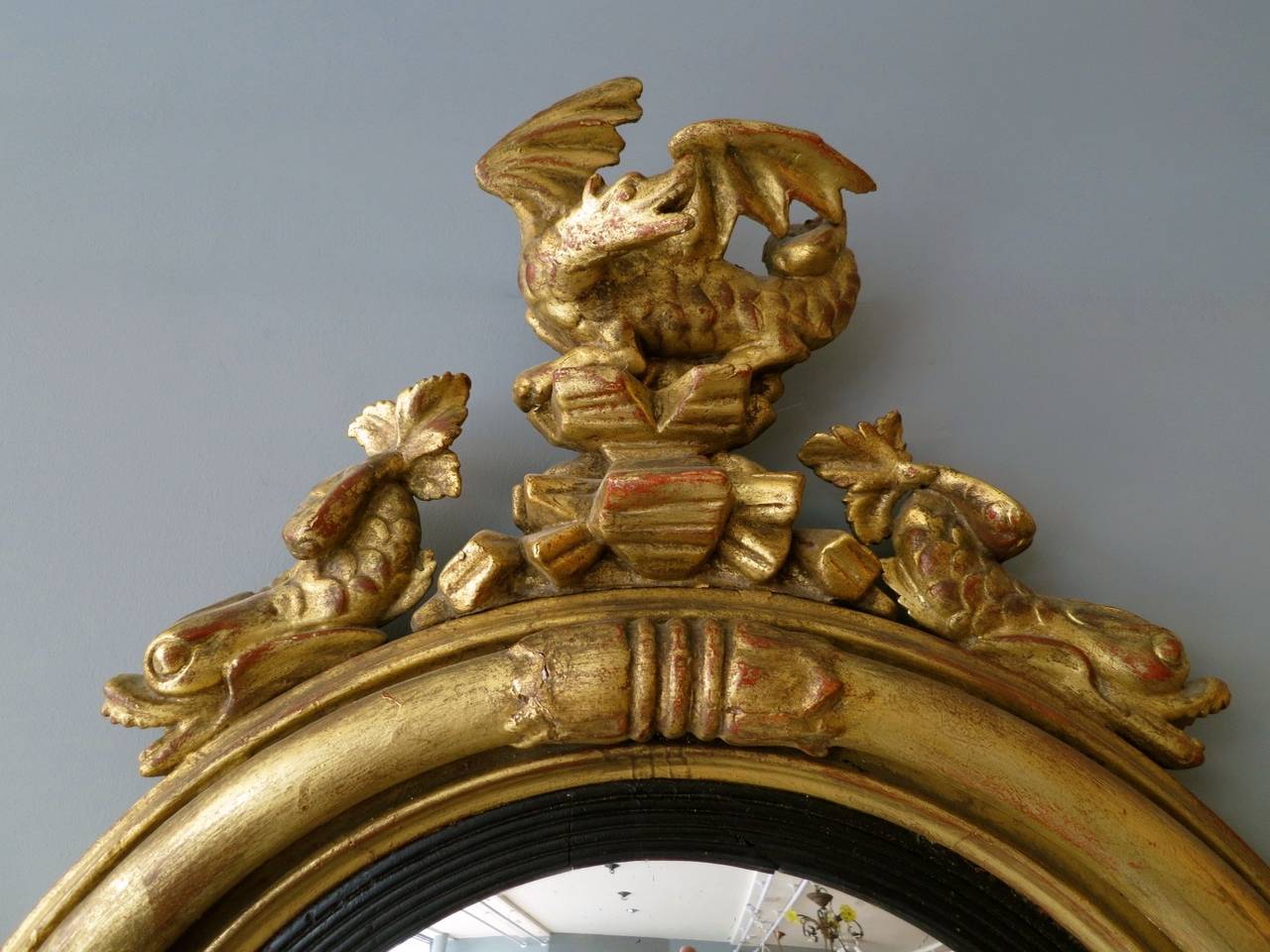 An English 19th century gilt convex mirror, crested by a dragon and two triton headed sea creatures and leaf decoration to bottom.