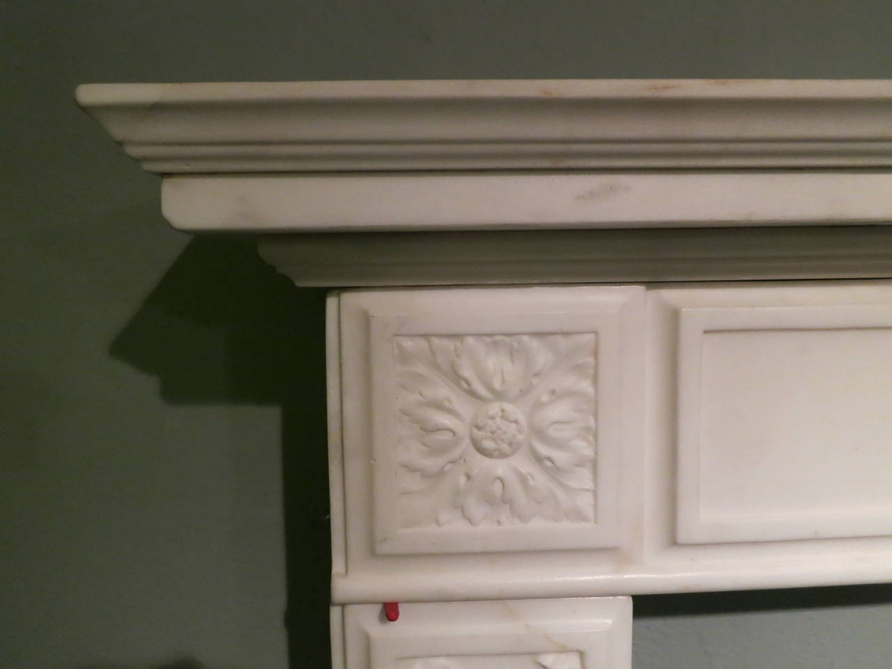 An Italian fireplace in statuary white marble. The jambs with carved bow tied foliage within a fielded panel, supporting a long running frieze with a carved centre scene of putti playing musical instruments in the heavens. They are flanked either