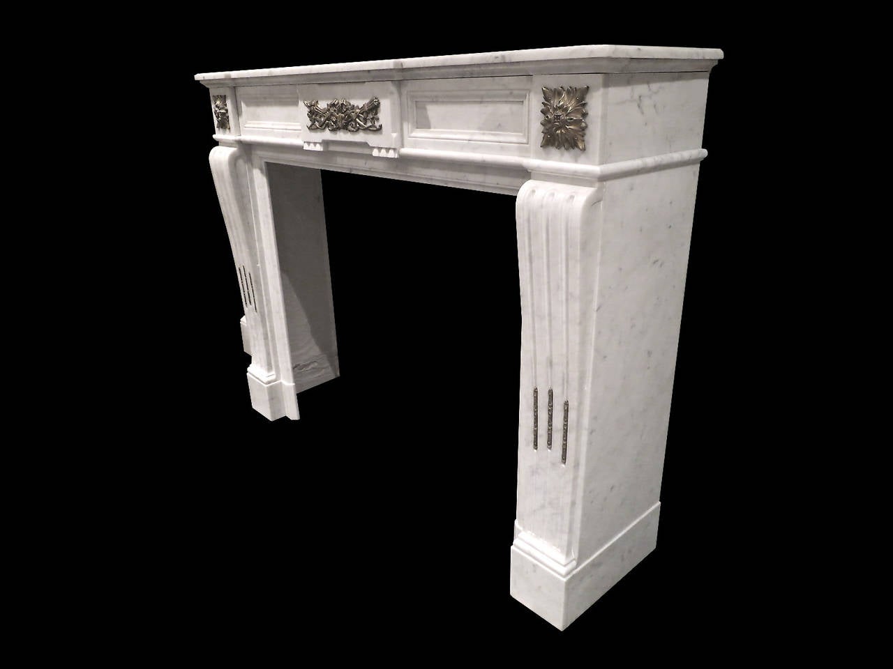 A 19th century Louis XVI style fireplace in pale Carrara marble with ormolu mounts. The fluted jambs decorated with Ormolu and surmounted by square ormolu patarae. The frieze having a centre tablet of Torch and Quiver in ormolu, flanked on either