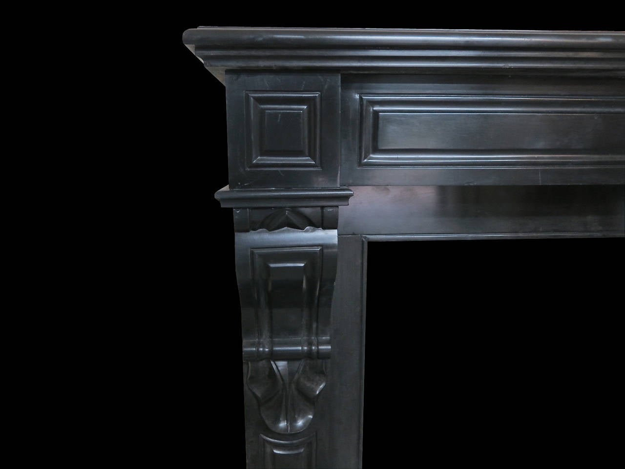 A petit and compact Louis XVI style fireplace in Belgian black marble. The paneled jambs surmounted by carved shells and paneled brackets. The conforming paneled frieze with square paneled corner blocks, all beneath a moulded and tiered shelf.