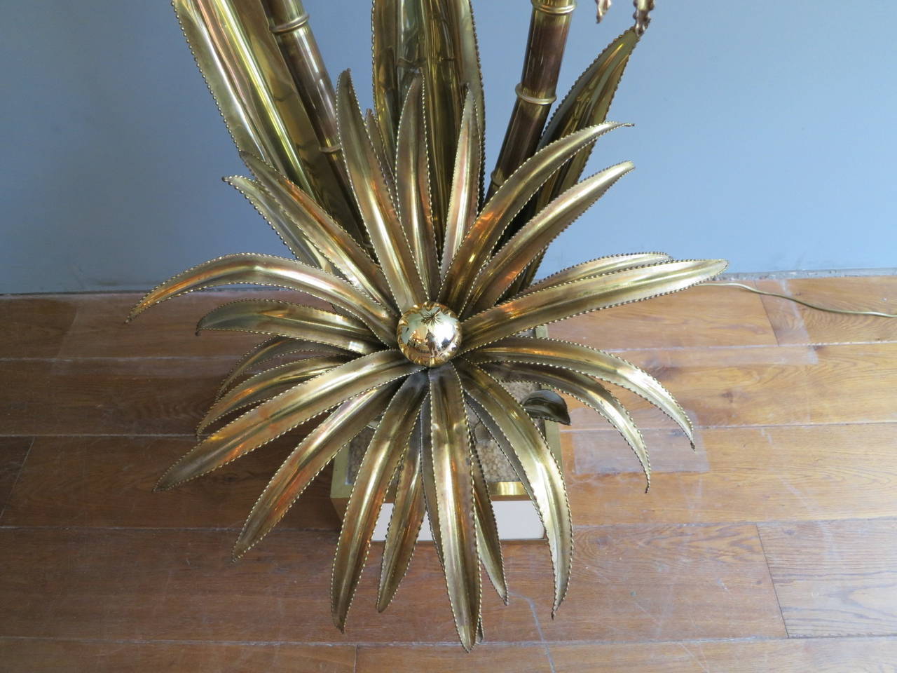 A tall three headed brass palm floor lamp with a white lacquered and brass base.
