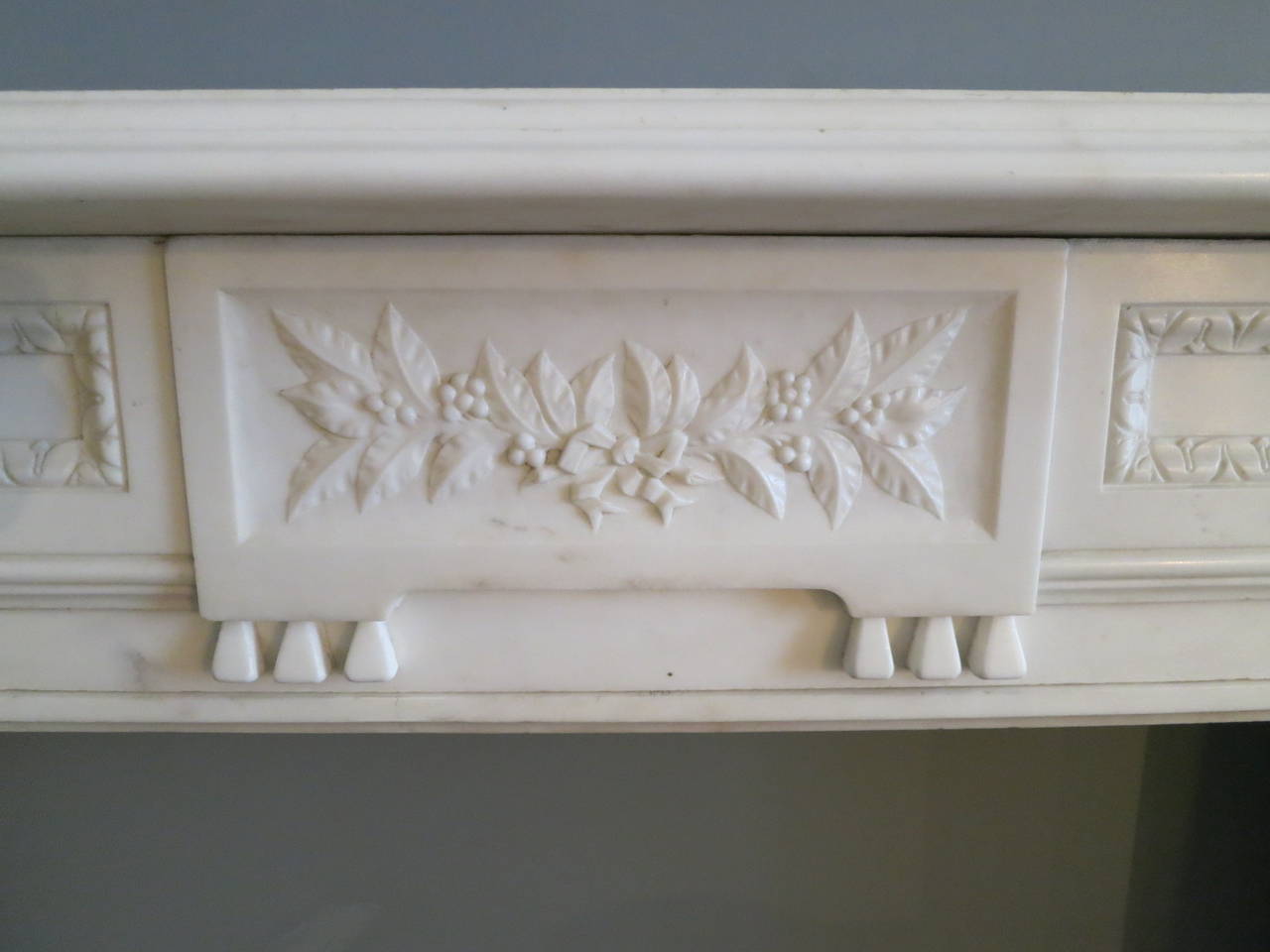 A substantial statuary white English marble fireplace in the Regency manner, the fluted jambs with cushion returns and carved floral corner blocks. The center tablet with carved floral tied spruce and berries, flanked on either side by foliage