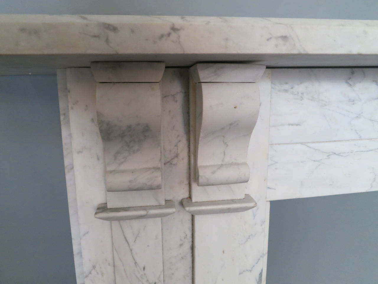 A large and imposing English William IV fireplace in pencil vein Carrara marble, with paneled pilaster jambs with twin corbel brackets supporting a long wide and generous mantel. Some minor restorations.

Measures: 96 cm H x 99 cm opening sizes.