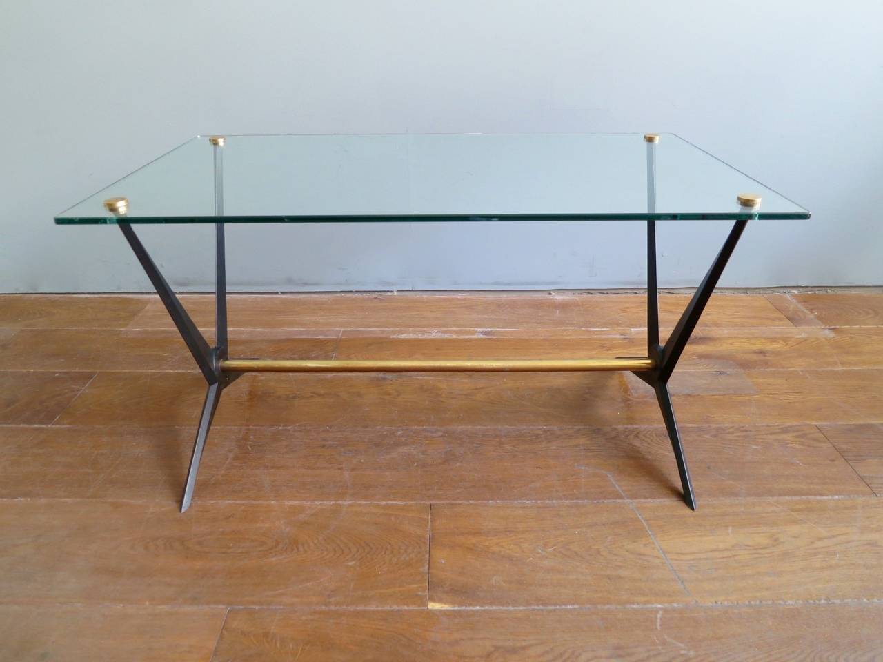 An Italian 1950s cocktail/coffee table with thick glass top with brass accents. The X-frame stretcher in brass and black steel again with decorative brass accents. By Angelo Ostuni 