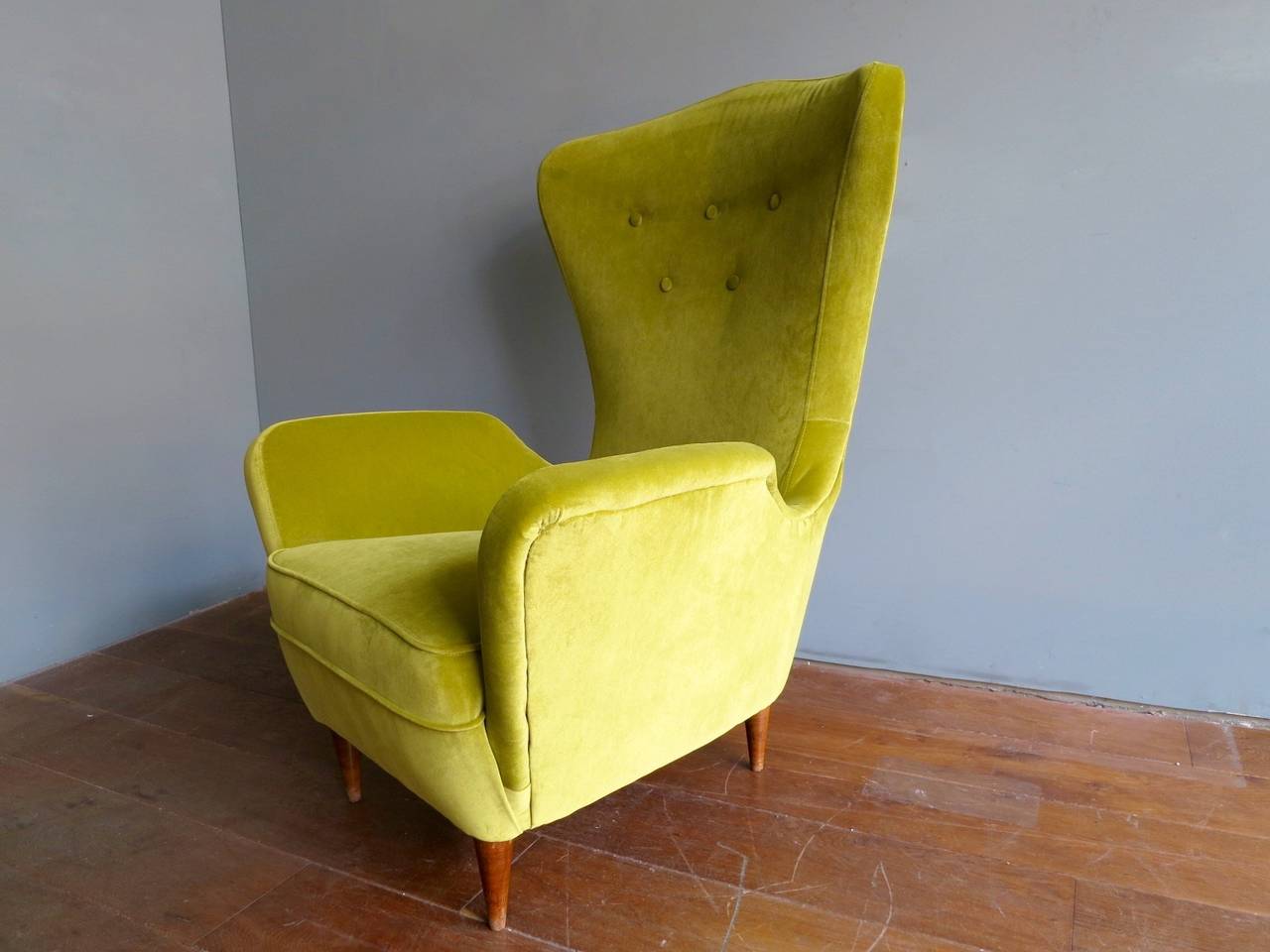 A wing backed Italian armchair reupholstered in pistachio colored moleskin velvet, on blonde wood conical supports.