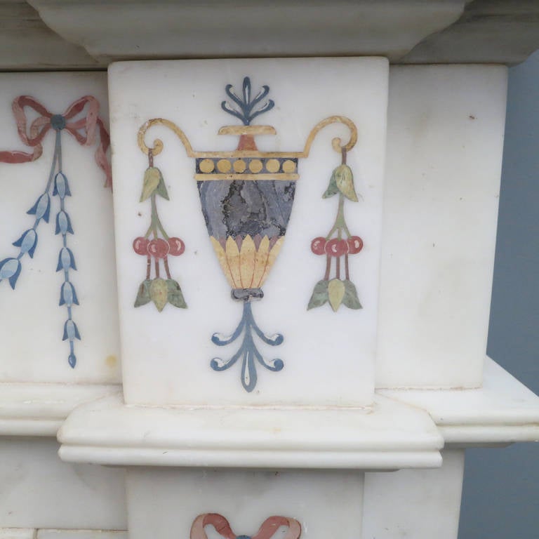 A white marble fireplace adorned with vibrantly colored inlays of classical figures, urns, ribbons, foliage and drapery. Surmounted by a molded and shaped shelf, early 20th century.