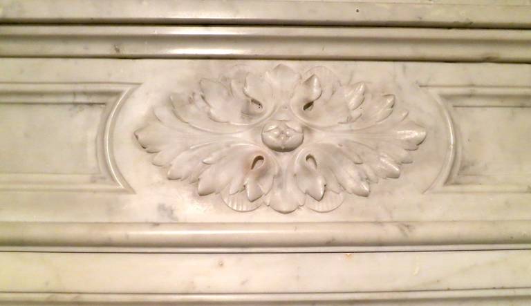 An antique 19th century French Louis XVI style fireplace in pale Carrara marble. Having demilune fluted jambs, surmounted by carved paterae corner blocks and the centre of frieze again with carved oval paterae. The shelf being shaped and molded.