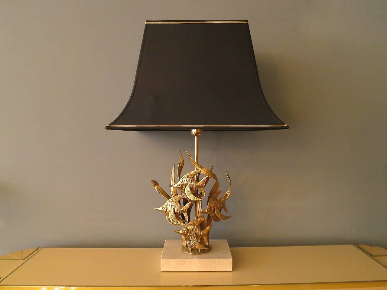 A large table lamp with gilt brass tropical fish on a travertine base with original black pagoda lampshade. Attributed to Maison Charles.