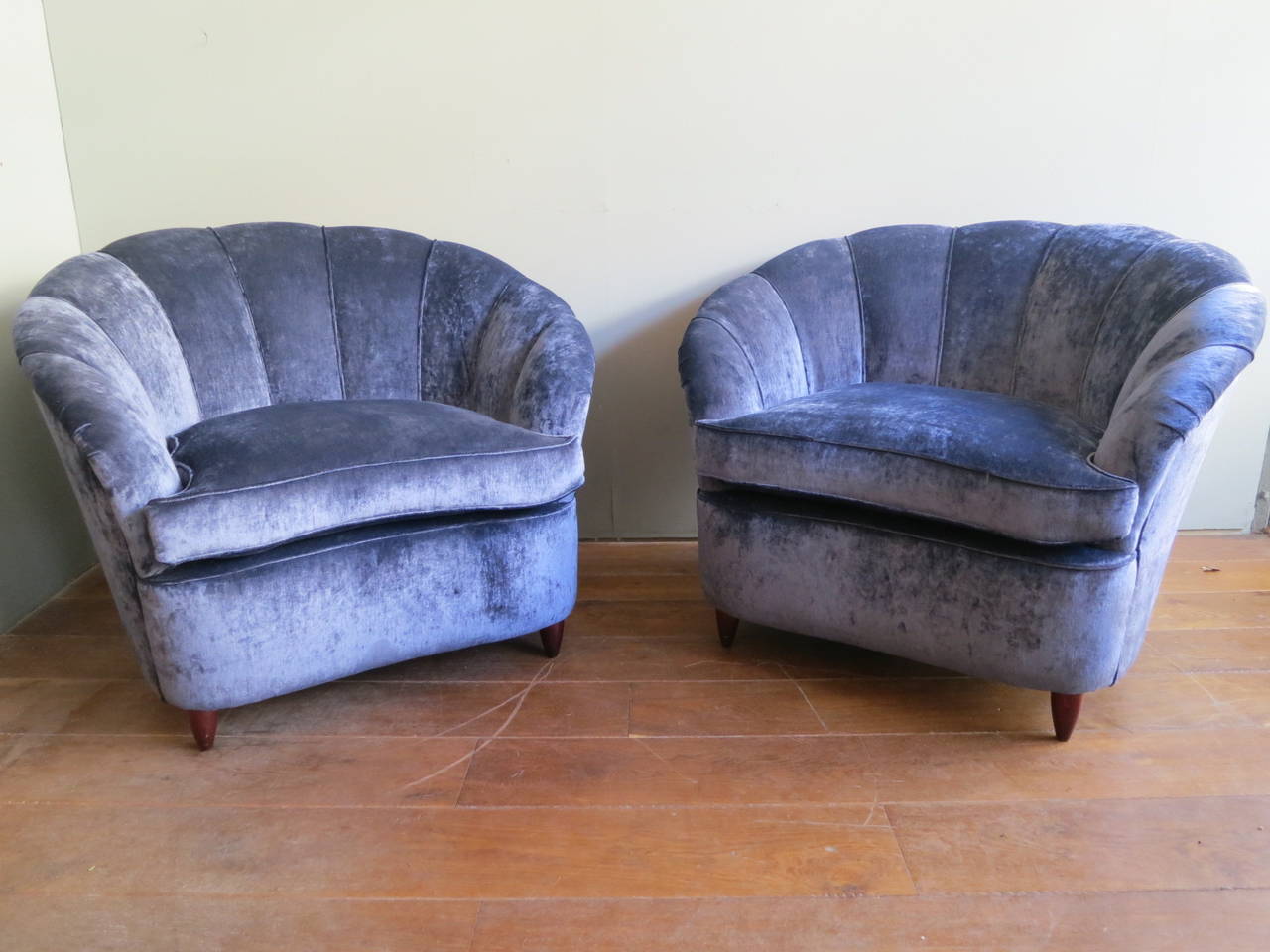 A pair of shell backed tub chairs, expertly reupholstered in crushed blue velvet on conical wooden feet.