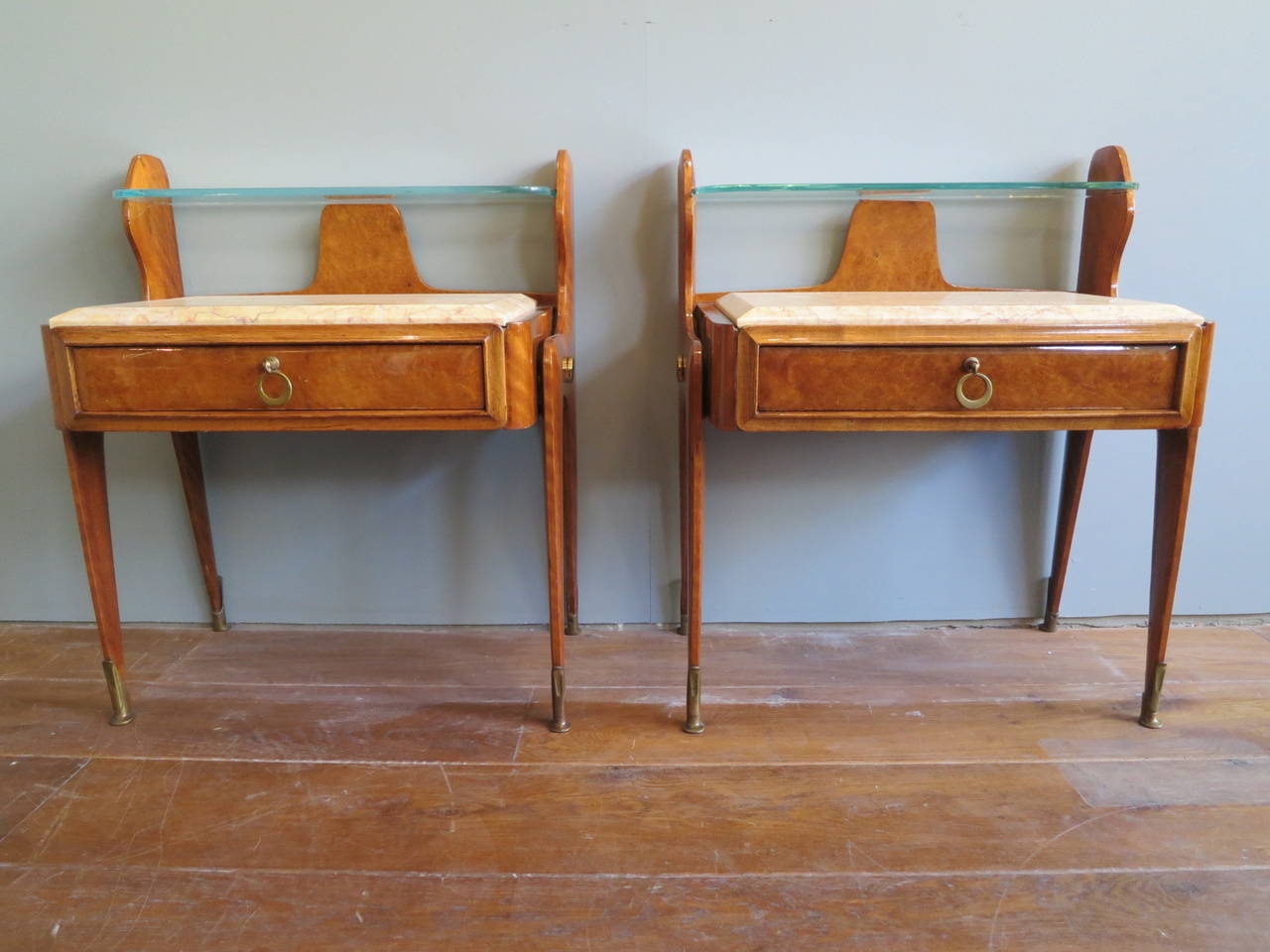 A pair of walnut and marble topped bedsides, with one draw, brass sabots and floating glass upper shelf.