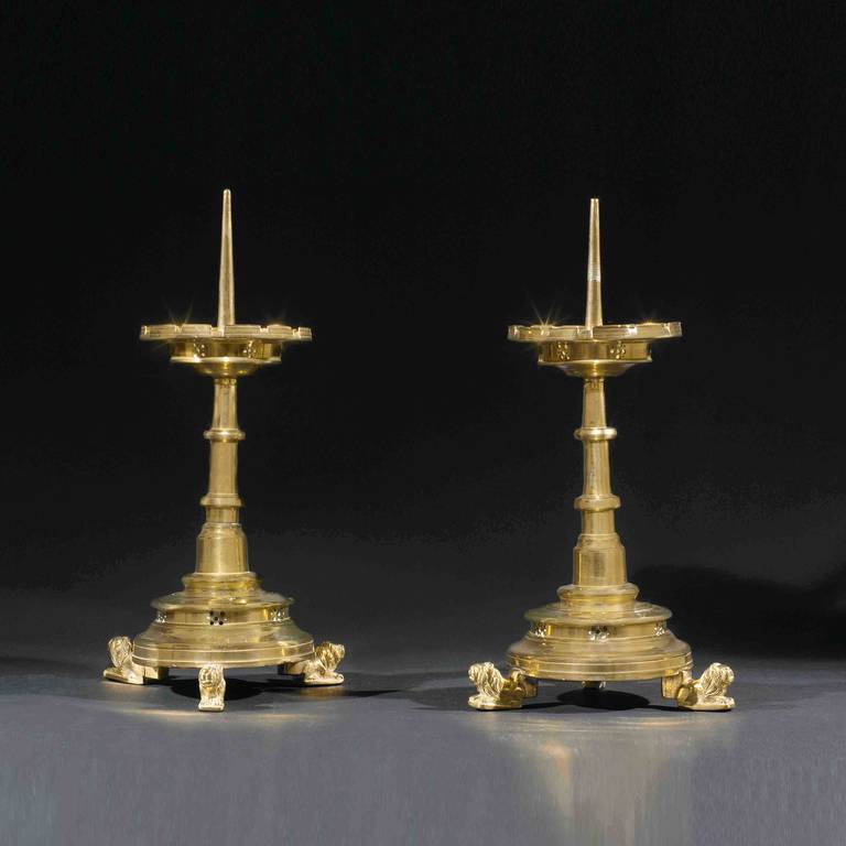 Pair of 15th century Flemish yellow brass candlesticks standing on three chiseled lions feet.
The base and the dish drip pan on top are pierced in a decorative manner and toothed all around the raised rim, reminding us of a castle with its